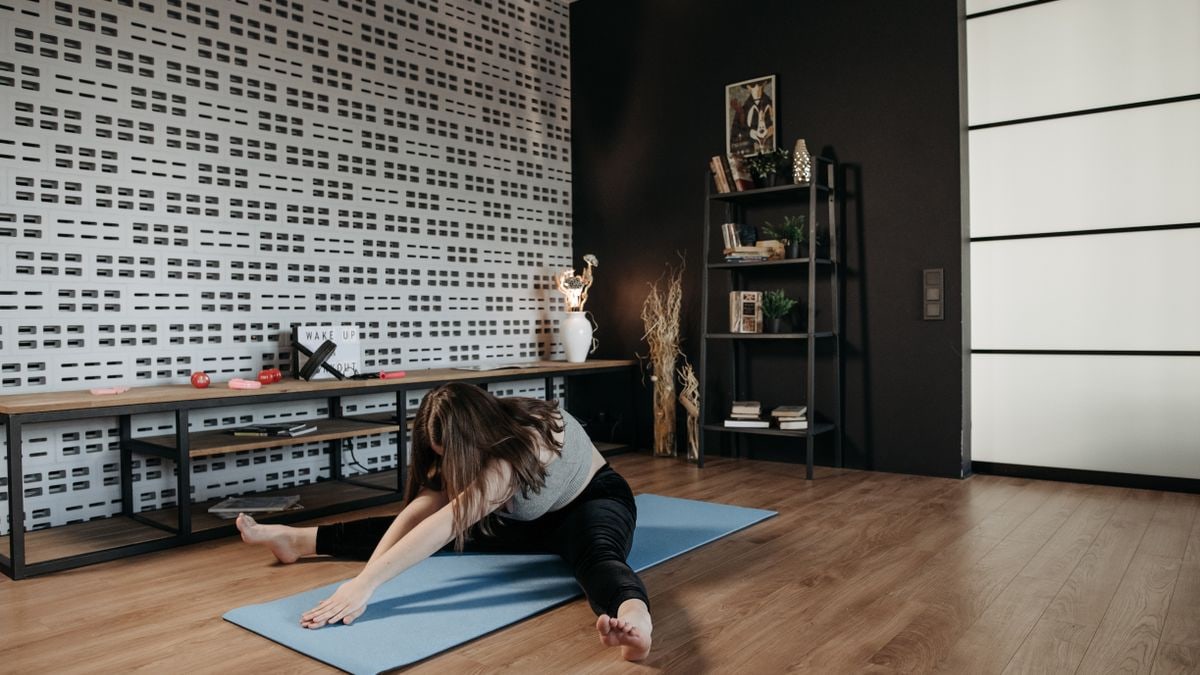 A woman performing a stretching exercise on a yoga mat in a stylish indoor space.
